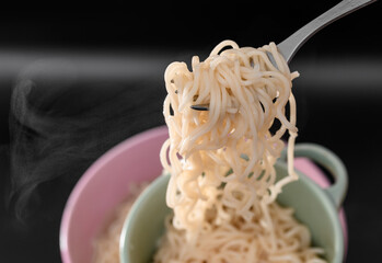 Ugotowany makaron spaghetti nakładany do miski na czarnym tle 