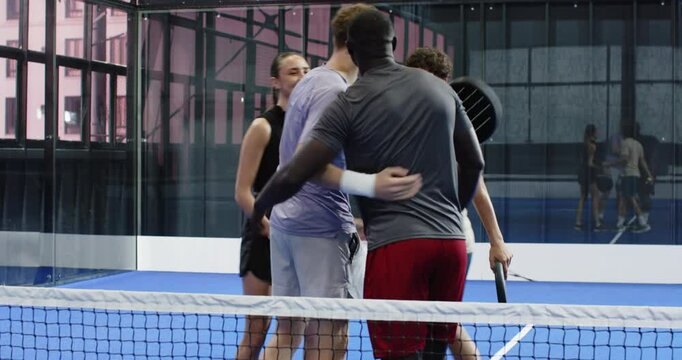 Diverse friends enjoying padel tennis match, laughing and chatting on court, on indoor court