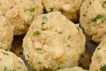 A round bread dumpling with visible specks of green herbs, surrounded by other dumplings