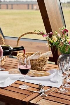 Red wine poured into glass beside fresh bread and flowers