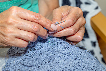 Close up of hands of unrecognizable woman knitting handmade clothes with spokes using  wool yarn....