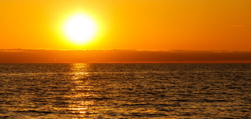 Obraz premium The sun is setting over the ocean, casting a warm glow on the water
