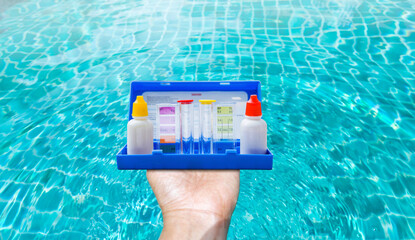 Water tester test kit in girl hand over blurred clear swimming pool water background, quality water...