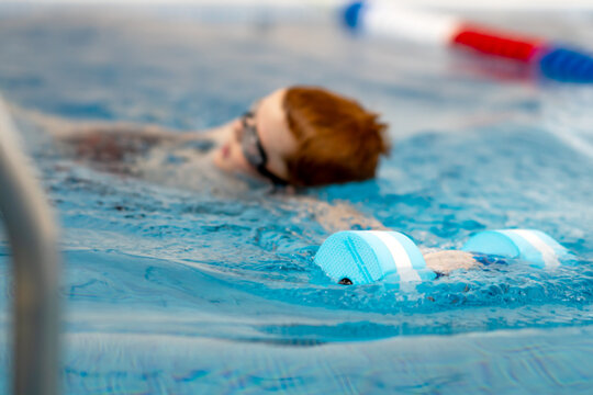 boy learns to swim. A boy in the pool will follow his coach. The child learns to swim crawl. Selective focus on swimming dumbbell