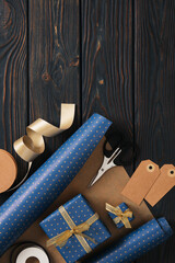 Supplies for gift wrapping. Wrapping paper, tags, and ribbon in blue and gold colors. Wooden background, space for your text.
