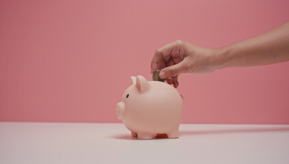 Close up of hand dropping an baht coin into a pink piggy bank. Financial and Business Safety Concept.