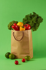 A paper grocery bag filled with fresh vegetables including kale, cauliflower, bell peppers,...