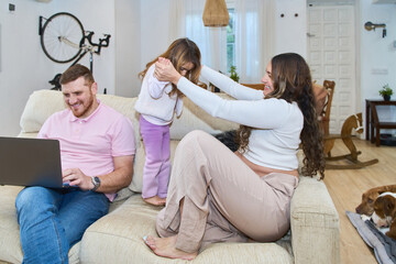 Fototapeta premium Pregnant mother playing with daughter while father works on laptop