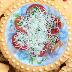 A plate of sliced tomatoes topped with shredded cheese and herbs, surrounded by cookies—perfect...