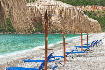 straw umbrella and sun loungers on a white pebble beach in Peloponnese Greece