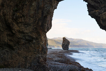 View of the beach by the ocean and cliffs through a stone arch. Island landscape