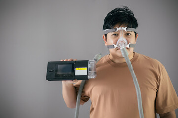 Man wearing and holding a CPAP machine while standing on a gray background
