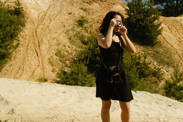 Woman tourist takes pictures of sand dunes with her retro camera during summer trip