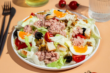Appetizing Salad with iceberg, tuna, boiled eggs in a white plate on the table. Healthy breakfast