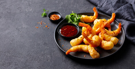 Shrimp tempura with sauce on a black plate. Grey background. Close up. Copy space.