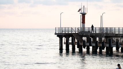 Solitary Person Standing on a Pier at Sunrise — Peaceful Seascape with Lighthouse Structure and Calm Waters