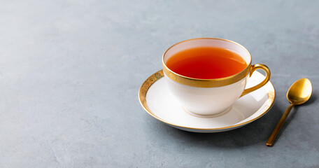 Tea in white cup with gold rim. Grey background. Close up. Copy space.