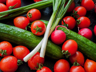 Fresh red cherry tomatoes, green leek, radish and cucumber on the black table background, top view of vegetables covered with water drops.