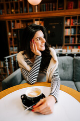 Young woman enjoying coffee in cozy cafe with bookshelves in background during daytime
