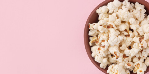 Tasty salty popcorn in a bowl on a pink background