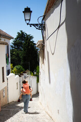 Mother carrying child on back walking up steep street in picturesque spanish town