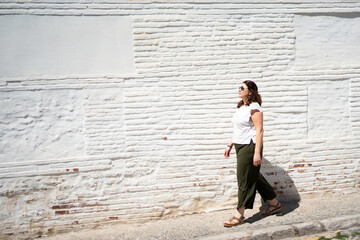 Tourist walking along white brick wall in sunny day