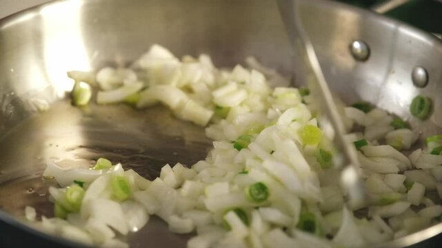 Chopped white onions and green onions browning in a pan, stirred by a chef