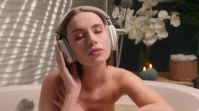 Caucasian female woman girl closed eyes listening music in waterproof headphones enjoying morning beauty procedure smooth skin at home bathroom relaxing listen audio melody song stress relief weekend