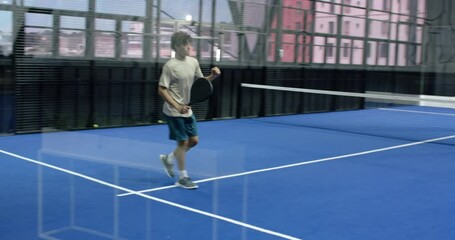 Young man playing padel tennis on indoor court, focusing on ball - Powered by Adobe