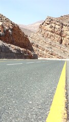 Ras Al Khaimah, UAE - March 26, 2025:Road curves beside monumental stone walls, their layers peeled...