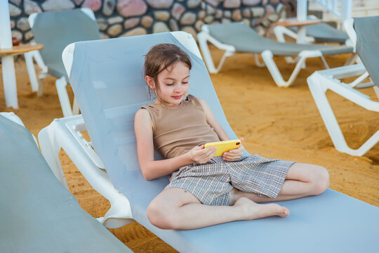Young girl relaxing on a poolside lounger using yellow smartphone while enjoying peaceful vacation time