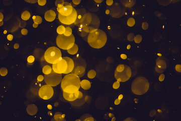 Defocused  golden bokeh lights in various sizes and colors on a dark background creating a dreamy and abstract visual effect