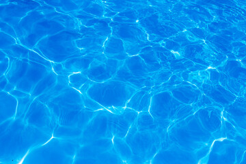 Clear blue swimming pool water surface with sunlight reflections creating abstract patterns and ripples, evoking a refreshing and tranquil summer vibe.