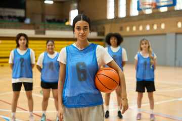 Female basketball player holding ball with teammates in background on court