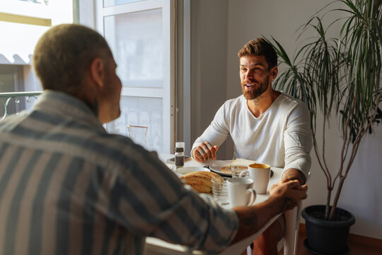 Gay couple holding hands and having breakfast at home - Powered by Adobe