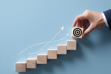 Hand placing block with target symbol on wooden steps illustrating growth and achievement in a professional setting