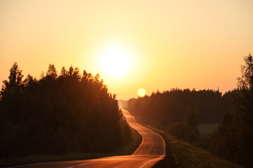 Bright sun at sunrise over the road and forest. Morning summer landscape at dawn