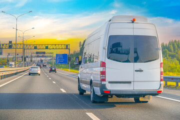 White mini bus is moving along city highway bypass road with beautiful sky before sunset. Fast express delivery transportation delivery passenger