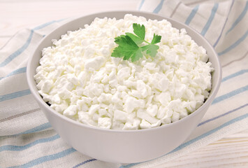 Farm cheese in a bowl on a light wooden background. Cottage cheese with parsley.