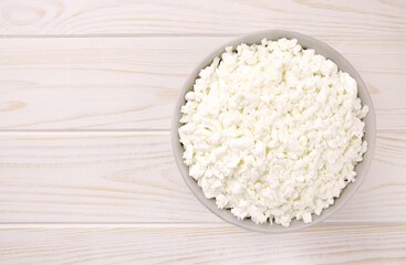 Farm cheese in a bowl on a light wooden background.