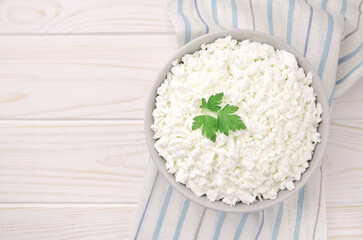 Farm cheese in a bowl on a light wooden background. Cottage cheese with parsley.