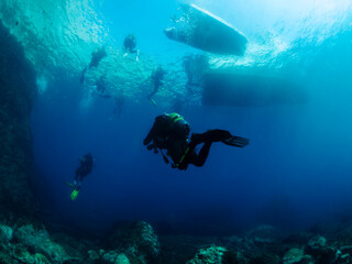 divers diving towards the boats on the sea surface, concept of scuba diving and underwater adventure