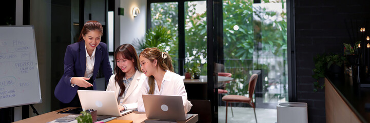 Asian Women Collaborate on Business Plan Using Laptop in Modern Office Teamwork Professional Meeting Brainstorming Project Strategy Startup
