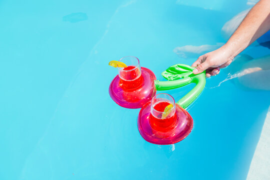 Cherry pool float with drinks in a sunny pool held by a man's hand