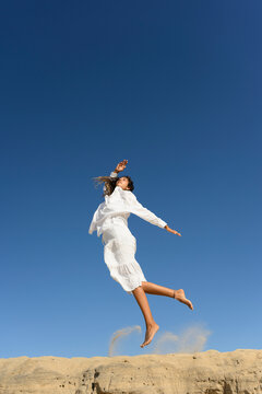 Woman in white dress jumping gracefully in a desert landscape under a clear blue sky