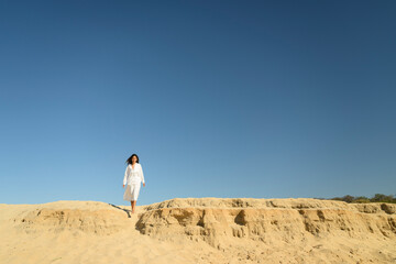 Woman in a white dress walking on a sand dune under a clear blue sky