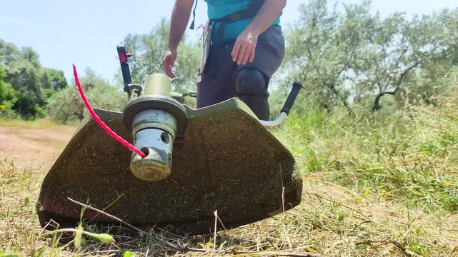 A field worker approaches to pick up his grass-cutting tool to attach it to his harness and begin the workday.