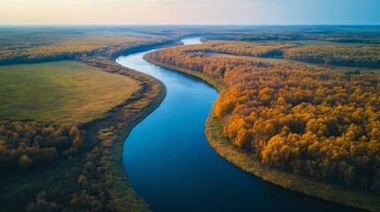 Vast fields stretch across the landscape, bordered by a graceful winding river. Autumn colors transform the scene with golden trees under a soft sunset glow, creating a tranquil atmosphere