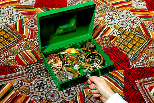 Hand opening a green box filled with jewelry on a colorful patterned fabric