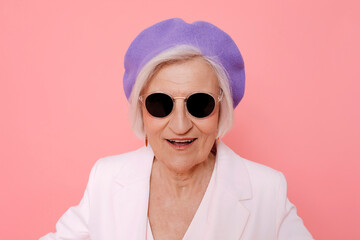 Fashionable woman in sunglasses and beret smiling against a pink background